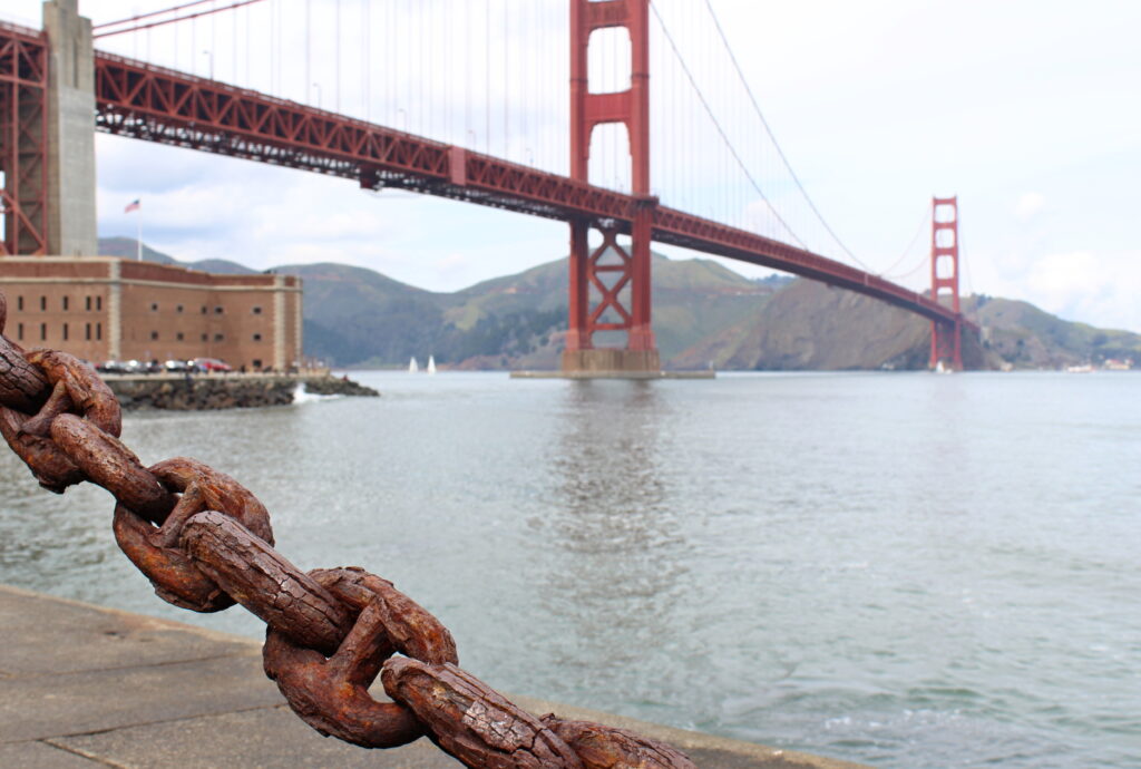 Pověstný most Golden Gate s řekou, v pozadí hory.