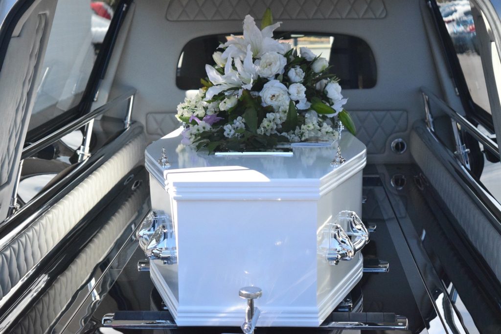 bílá rakev s květinovou ozdobou uvnitř pohřebního auta