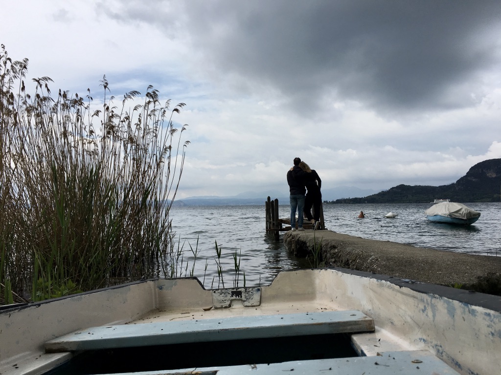Barča a Marco u jezera, zatažená obloha a v popředí loďka