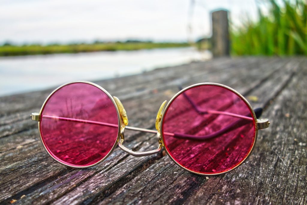 Růžové kulaté brýle, ležící na molu u rybníka.