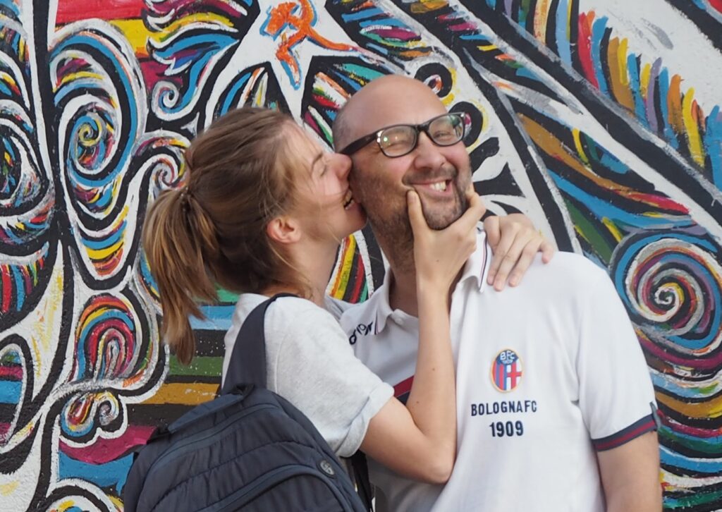 Denisa dává pusu svému Marcovi, v pozadí je vidět barevná zeď ve stylu street art.