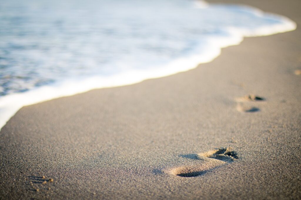 Stopy v písku na pláži, přímo u břehu.