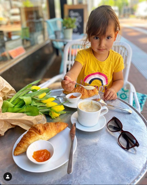 Dcera Heleny na snídani venku, na stole croissanty a tulipány.